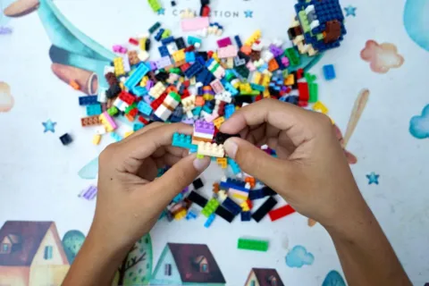 Anak laki-laki sedang menyusun balok kayu warna-warni sebagai permainan edukatif anak