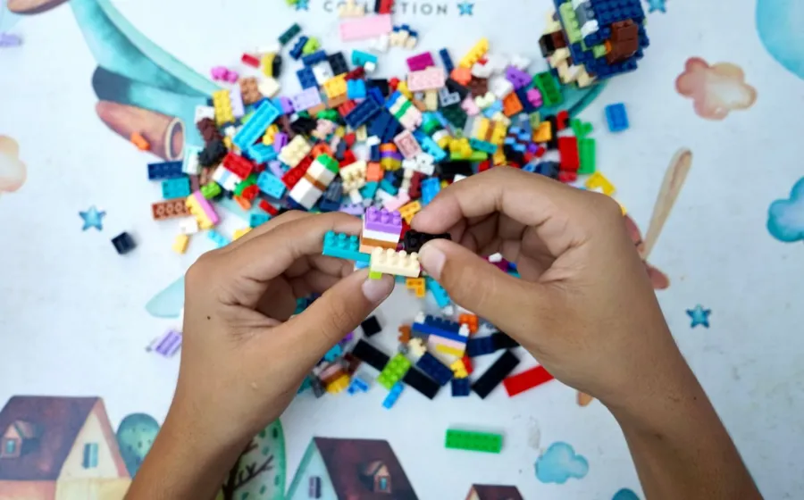 Anak laki-laki sedang menyusun balok kayu warna-warni sebagai permainan edukatif anak