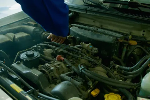 Mekanik sedang menuangkan oli kendaraan baru ke dalam mesin mobil untuk perawatan rutin.