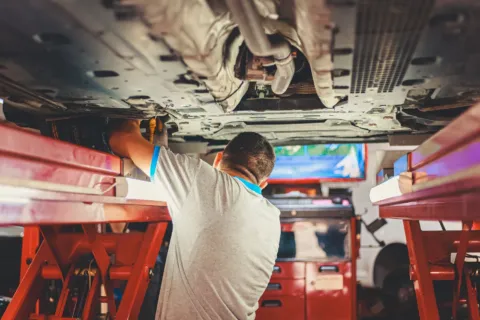 Mekanik sedang melakukan inspeksi mesin dalam tips merawat mobil bekas agar tetap prima