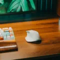 Pengguna sedang menggenggam mouse ergonomis nirkabel di atas meja kerja yang rapi