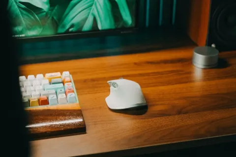 Pengguna sedang menggenggam mouse ergonomis nirkabel di atas meja kerja yang rapi