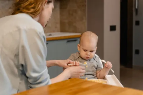 Anak balita duduk di kursi makan menghadapi piring berisi makanan sehat sebagai tips mengatasi anak susah makan