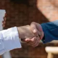 Dua profesional saling berjabat tangan saat membahas cara membangun hubungan bisnis di kafe