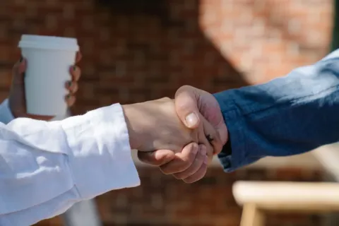 Dua profesional saling berjabat tangan saat membahas cara membangun hubungan bisnis di kafe