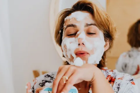 Ilustrasi cara membersihkan wajah dengan mengusapkan air hangat secara lembut di kamar mandi