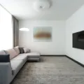 Ruang tamu mungil yang rapi dan terang dengan cermin dinding serta sofa berkaki ramping agar rumah terlihat luas