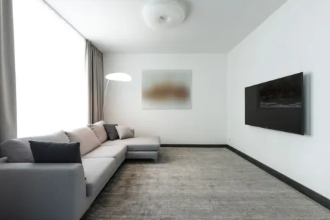 Ruang tamu mungil yang rapi dan terang dengan cermin dinding serta sofa berkaki ramping agar rumah terlihat luas