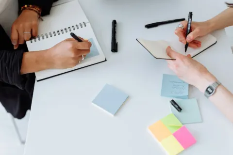 Seseorang menulis catatan untuk mempelajari cara mencari ide bisnis di buku agenda