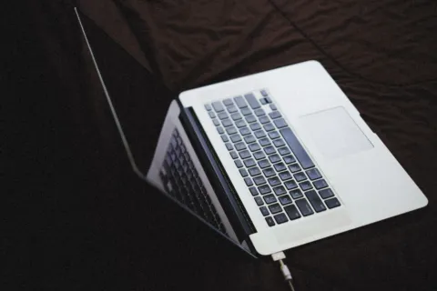 Seseorang sedang mengisi daya baterai laptop di atas meja kerja yang rapi