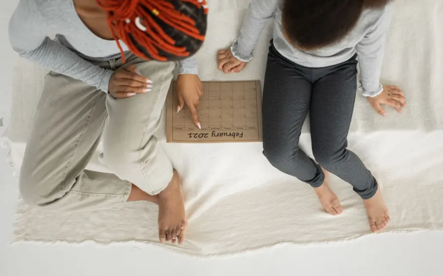 Ibu dan anak sedang menempelkan stiker kegiatan pada papan tips membuat jadwal anak di rumah